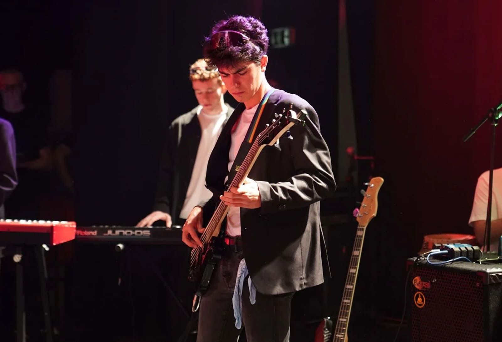 Studenti della Scuola e Accademia di Musica Cluster durante una performance dal vivo: chitarrista in primo piano, tastierista e strumentazione professionale sullo sfondo