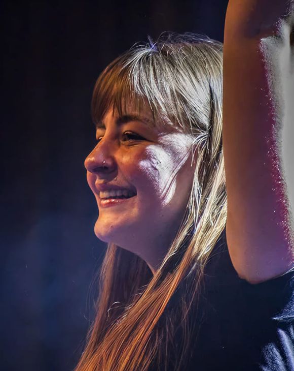 Studentessa della Scuola e Accademia di Musica Cluster sul palco durante una performance dal vivo, con espressione sorridente e braccio alzato sotto le luci sceniche