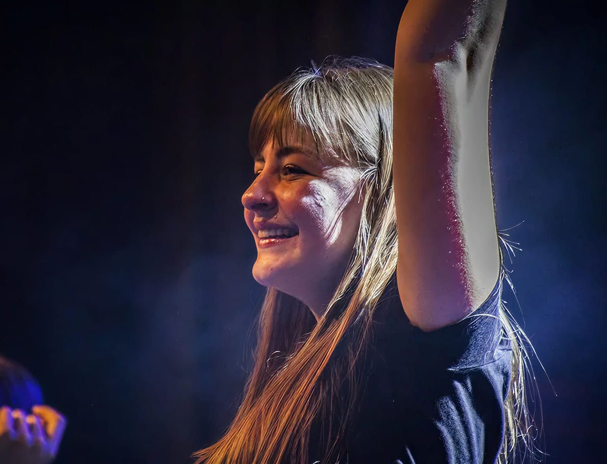 Studentessa della Scuola e Accademia di Musica Cluster sul palco durante una performance dal vivo, con espressione sorridente e braccio alzato sotto le luci sceniche